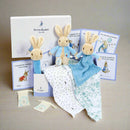 Baby gift set with Peter Rabbit plush toys, blanket, and cards on a white background
